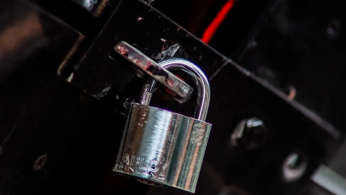 Zbliżenie metalowej kłódki marki Abloy zapiętej na czarnych drzwiczkach z czerwonym akcentem