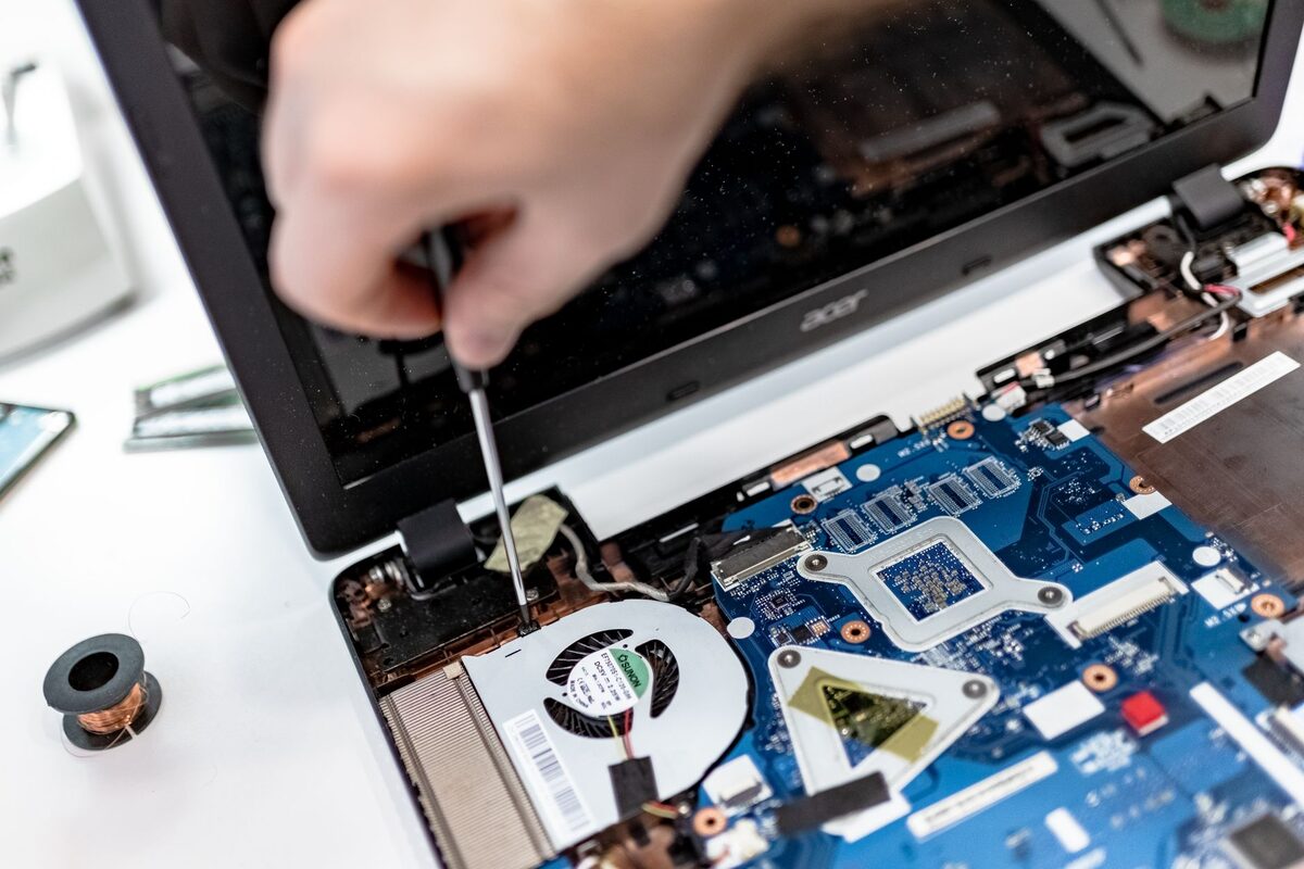 Dłoń odkręcająca śrubokrętem obudowę laptopa podczas naprawy w domu klienta